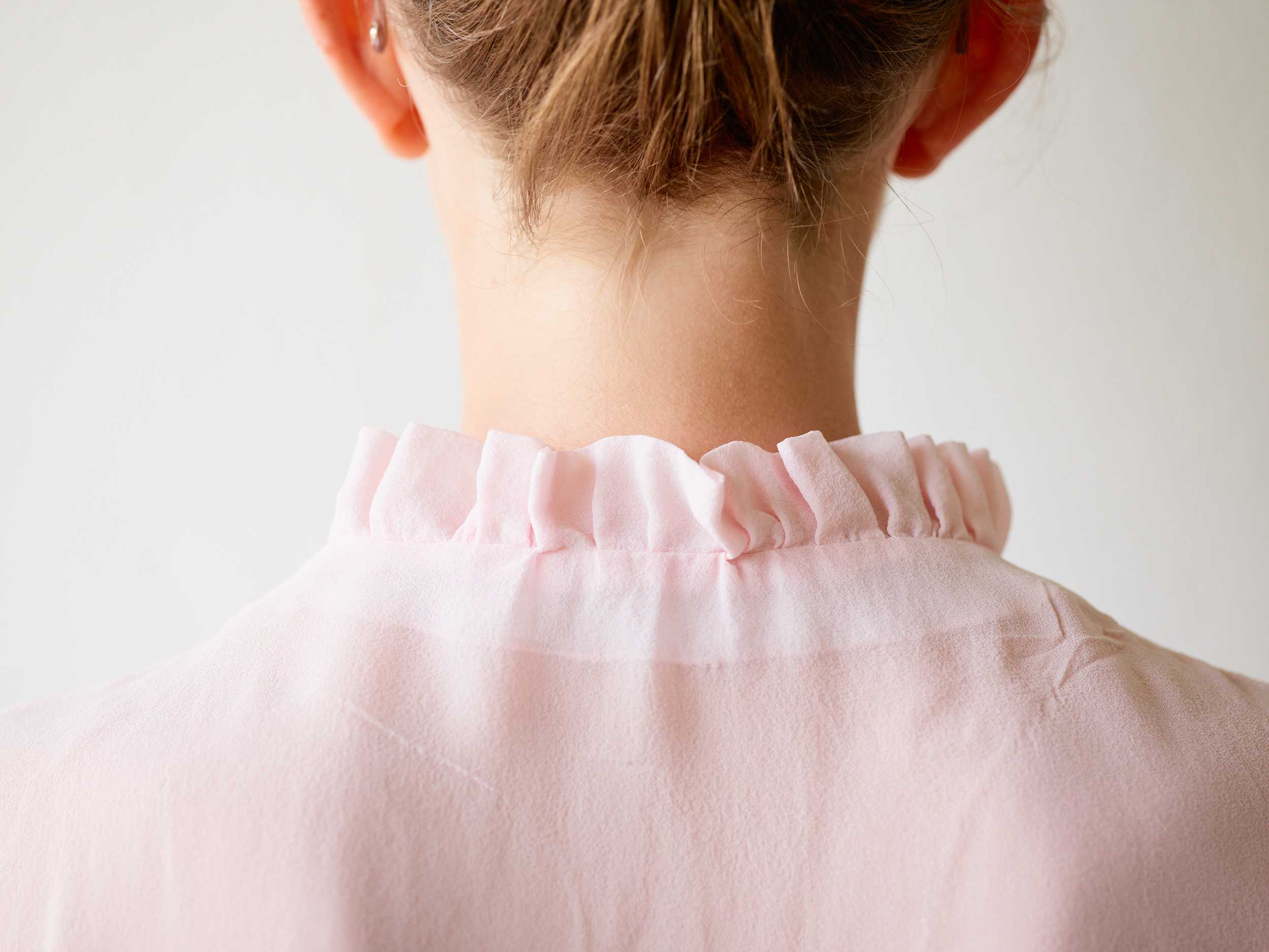 Back view of a person wearing a light pink blouse with a ruffled collar